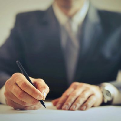 Male entrepreneur wearing formal suit sitting at table in workplace and signing documents while making successful business deal